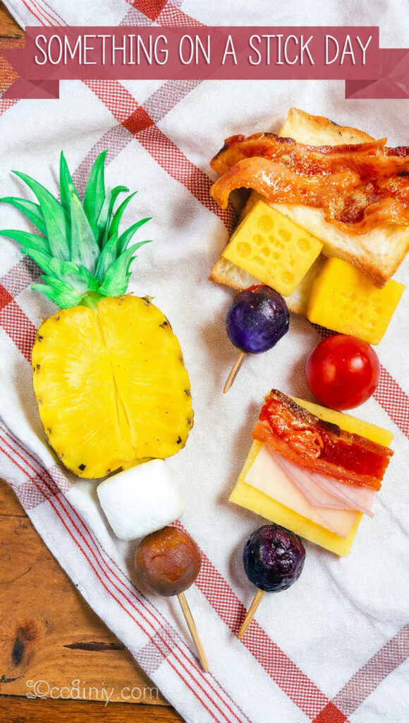 「Something on a Stick Day」というタイトル入りの画像。チェック柄の布の上に、パイナップルとマシュマロの串、ベーコンとチーズとトーストの串など、手軽な軽食が並んでいる。